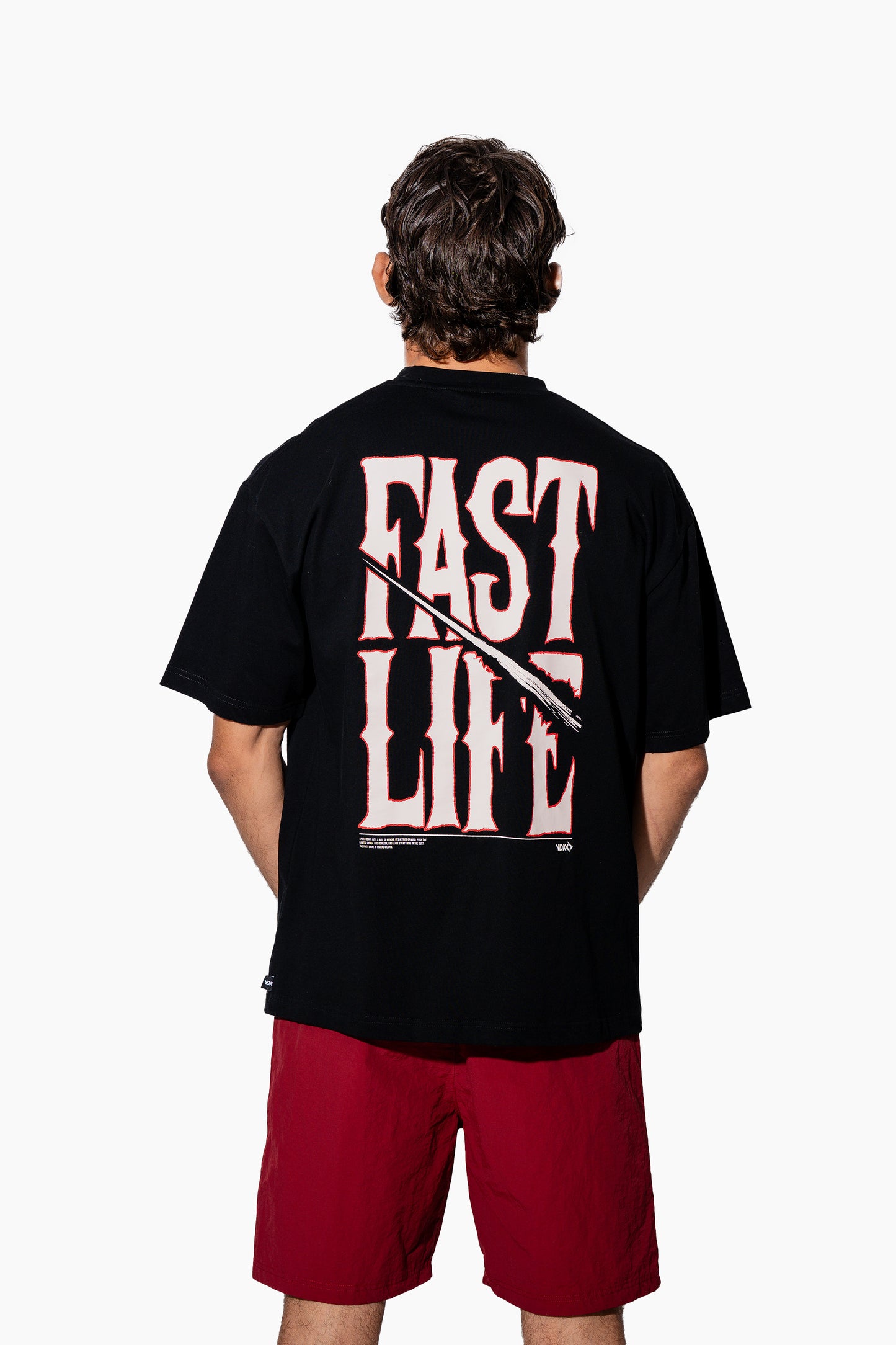 Man wearing a black t-shirt with FAST LIFE on it and red shorts on a white background