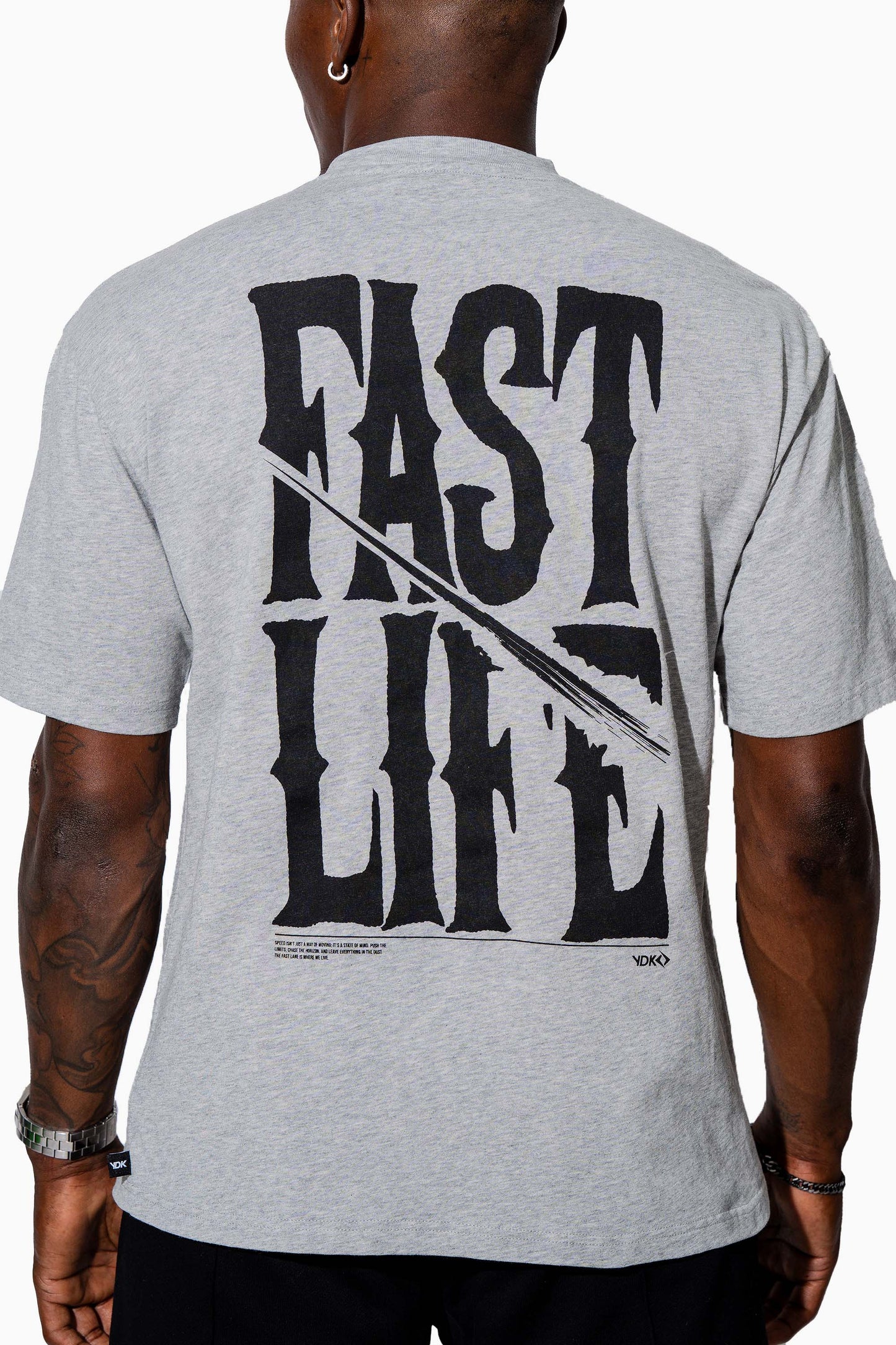 Man wearing a grey marl t-shirt with FAST LIFE on it and black pants on a white background