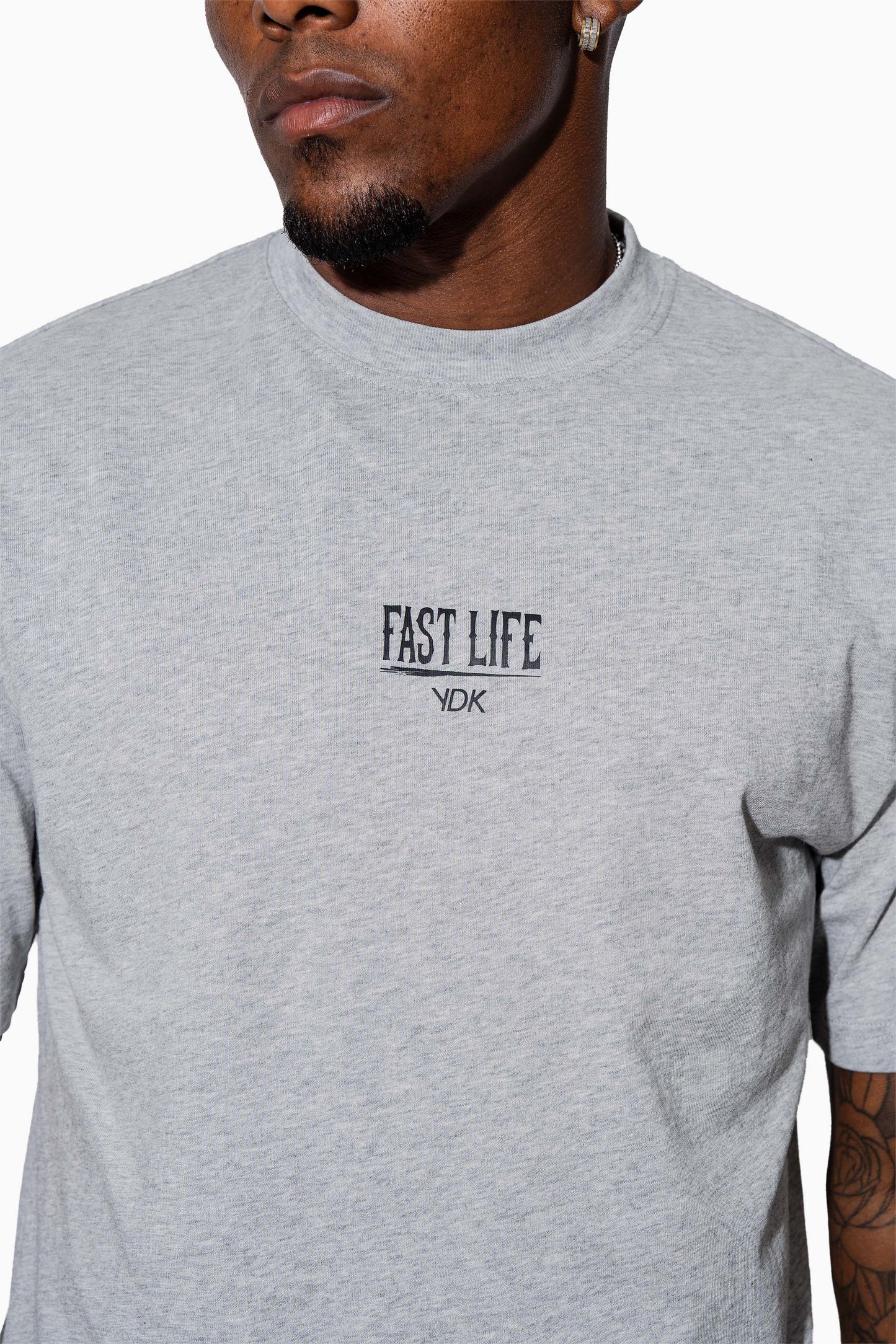 Man wearing a grey marl t-shirt with FAST LIFE on it and black pants on a white background