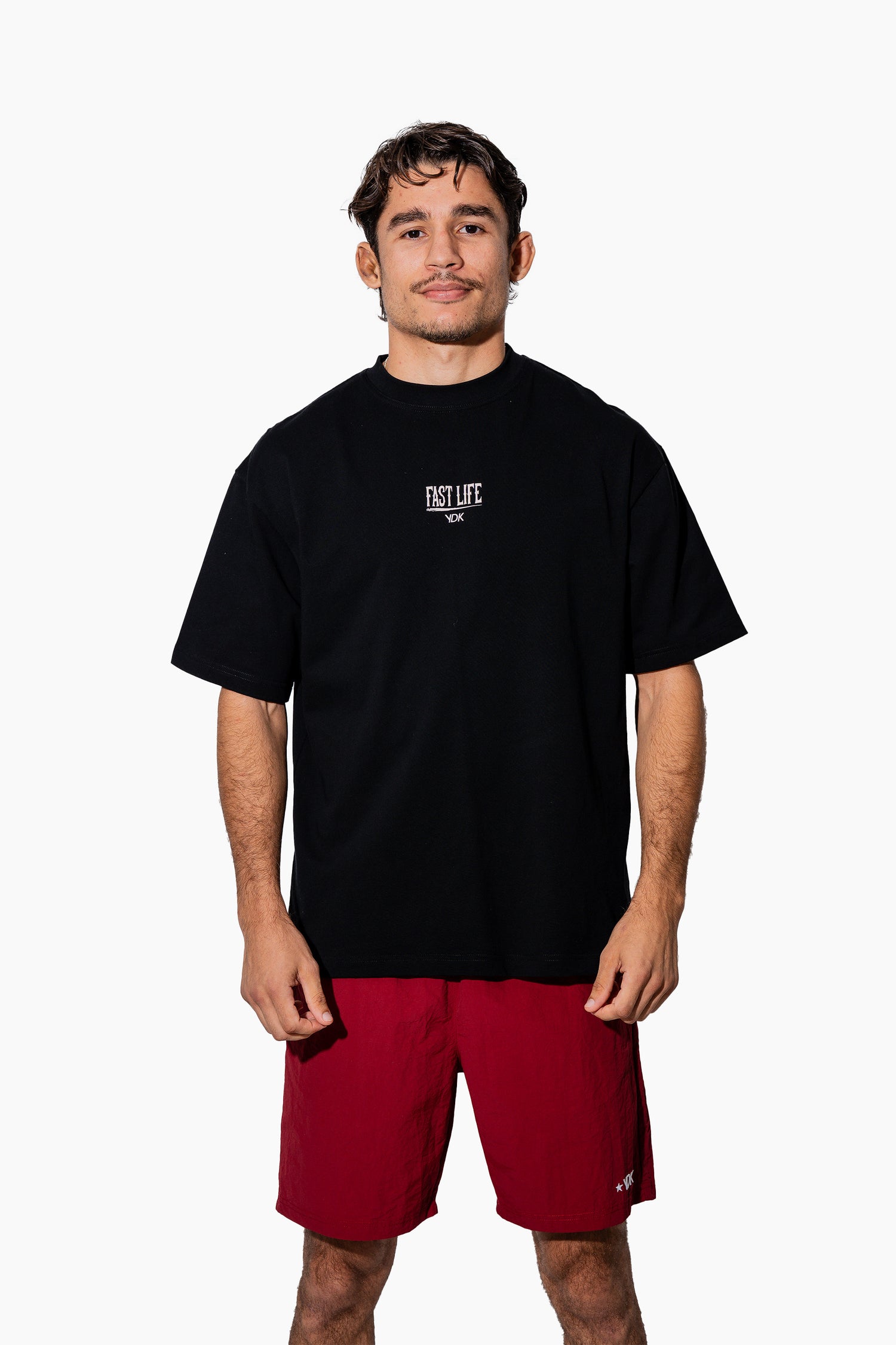 Man wearing a black t-shirt with FAST LIFE on it and red shorts on a white background