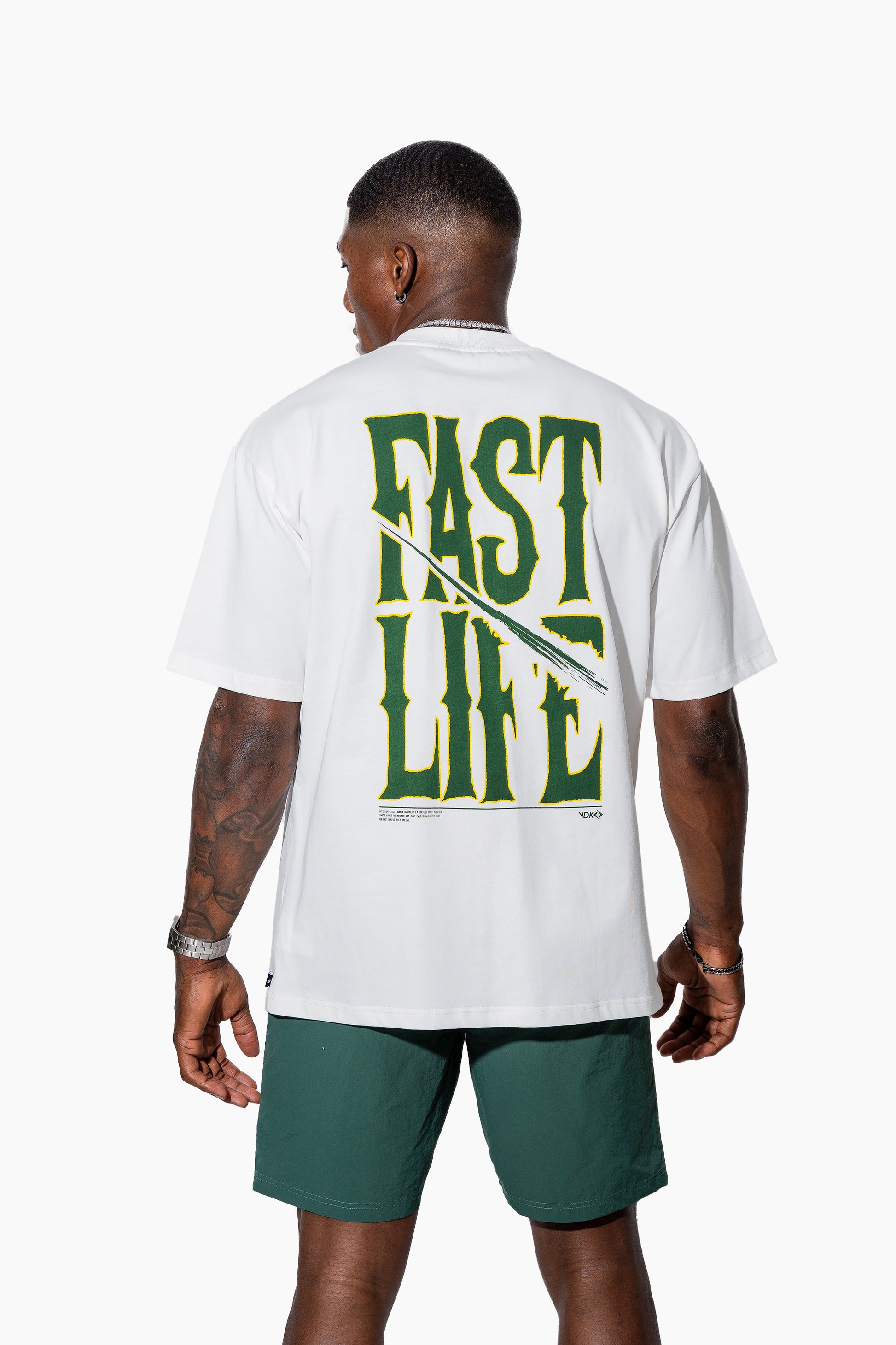 Man wearing an off-white t-shirt with FAST LIFE on it and green shorts on a white background