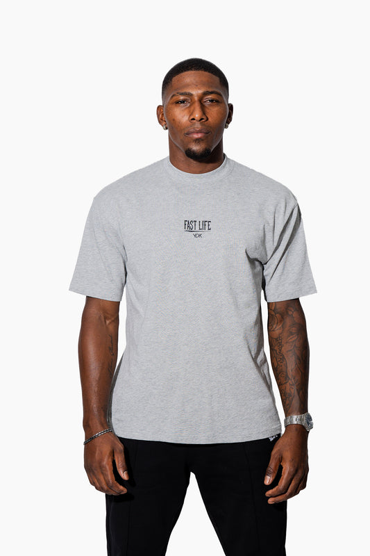 Man wearing a grey marl t-shirt with FAST LIFE on it and black pants on a white background